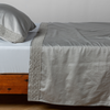 Bria Flat Sheet | Cotton sateen sleeping pillow and flat sheet embellished with cotton lace trim on a bed - side view.