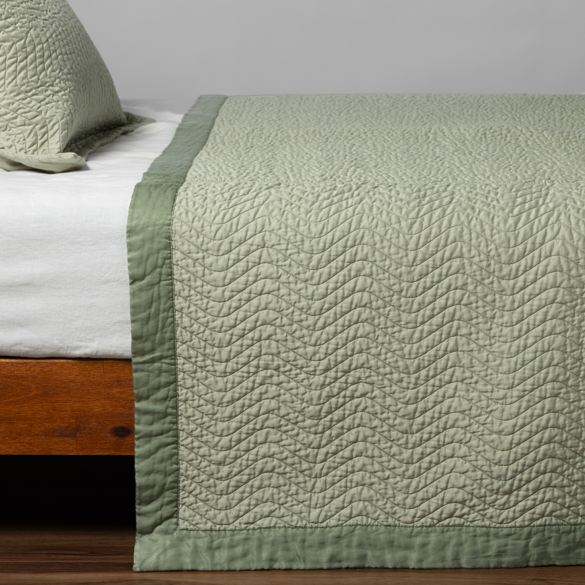 Cirillo Coverlet | Desert Sage | matching cirillo bedspread and sham in desert sage, a serenely elegant green, offering a hushed hue, shown from the side on a bed against a plain background.