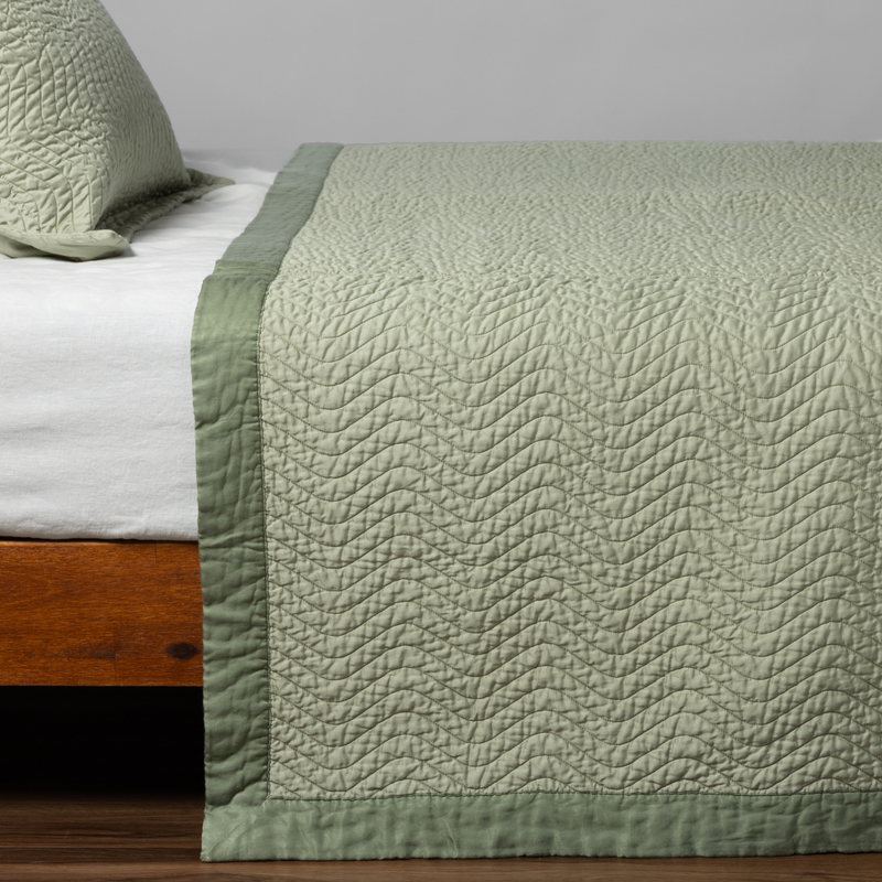 Cirillo Coverlet | Desert Sage | matching cirillo bedspread and sham in desert sage, a serenely elegant green, offering a hushed hue, shown from the side on a bed against a plain background.