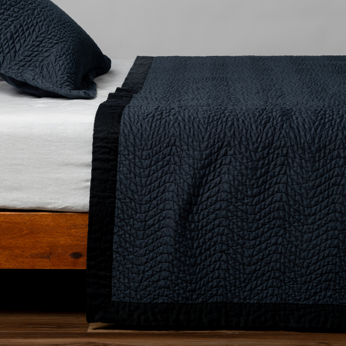 Cirillo Coverlet | Slate | Matching Cirillo Bedspread and Sham  in slate, a polished dusky dark blue, shown as the sideview on a bed against a plain background.