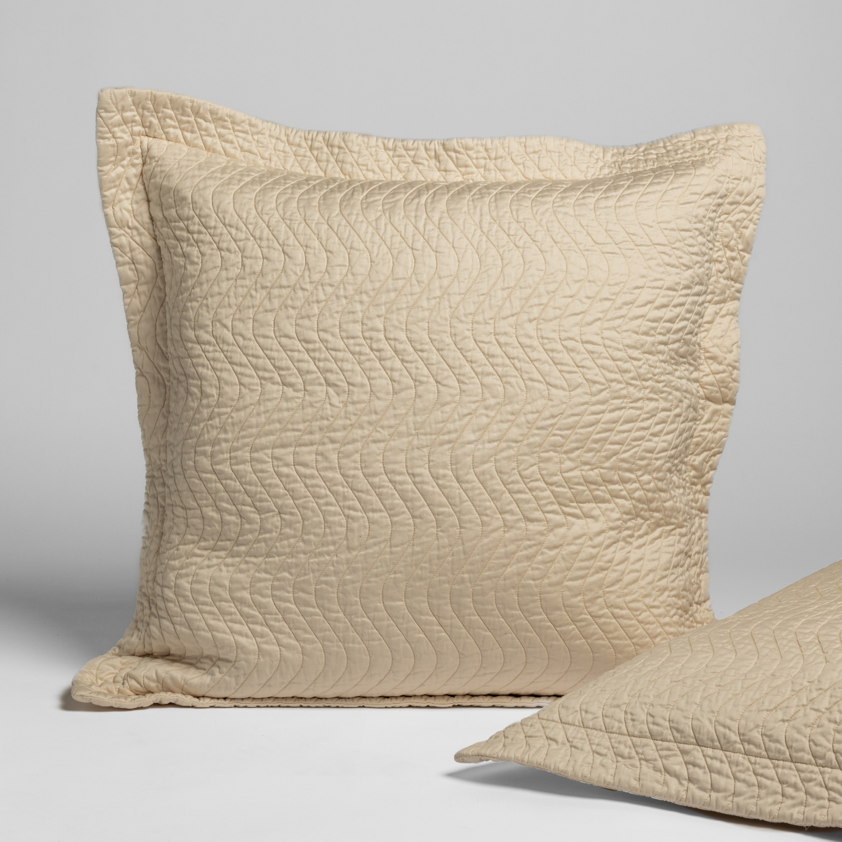 Cirillo Sham | Natural | quilted cotton sateen pair of shams, one upright and one on its side against a plain background.