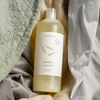 a bottle of unscented common good laundry detergent nested in linen and cotton fabrics in various colors.