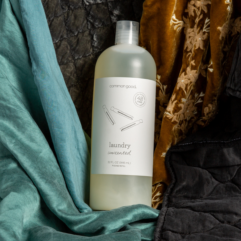 a bottle of unscented common good laundry detergent nested in charmeuse and silk velvet fabrics in various colors.