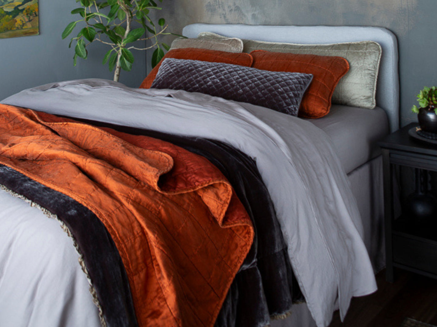A bed dressed with Sel Throw Pillows in Moonlight (18x54 & 18x18) and Silk Velvet Quilted Throw Pillow (16x36) in Moonlight with Sel Shams in Autumn on a bed layered with Madera Luxe Sheets and Duvet Cover in Moonlight. Carmen Blanket at the bed end and Sel Throw Blanket in Autumn, finished with the Austin Bed Skirt in Moonlight. 