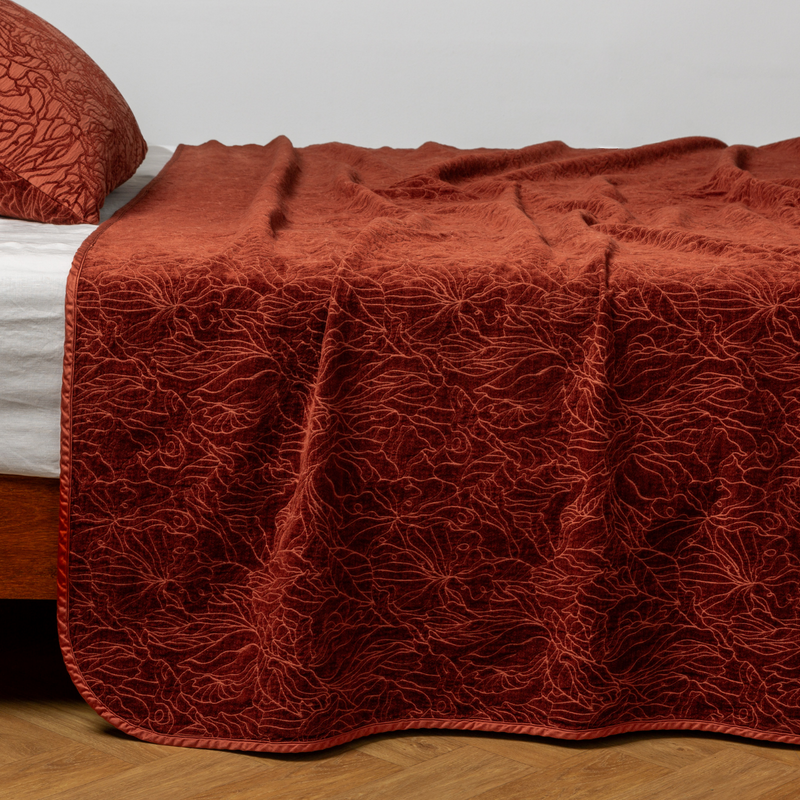 Autumn | A close-up side view of a bed with our Georgia Bedspread on its chenille jacquard side and a matching pillowcase on its cotton jacquard side in Autumn, a rich terracotta tone.