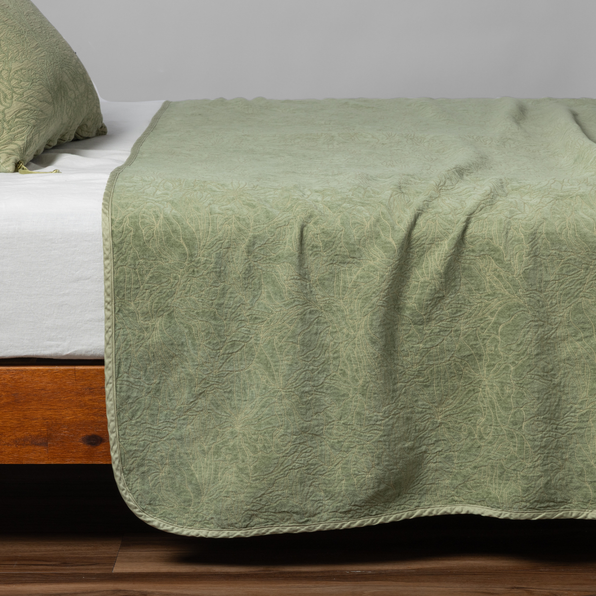 Georgia Twin Bedspread | Desert Sage | matching georgia bedspread and sham in desert sage, a serenely elegant green, offering a hushed hue, shown from the side on a bed against a plain background.
