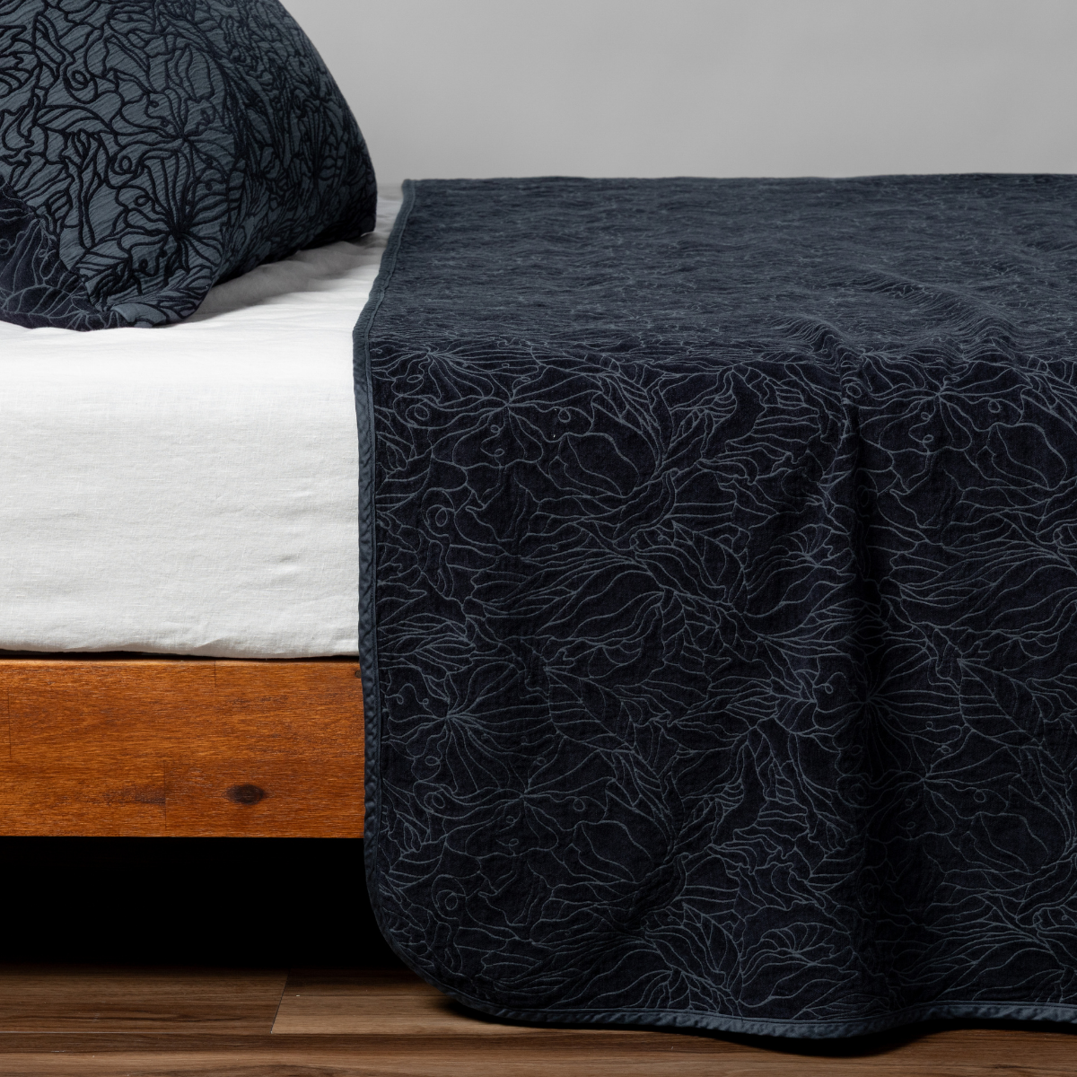 Georgia Twin Bedspread | Slate | Matching Georgia Bedspread and Sham  in slate, a polished dusky dark blue, shown as the sideview on a bed against a plain background.