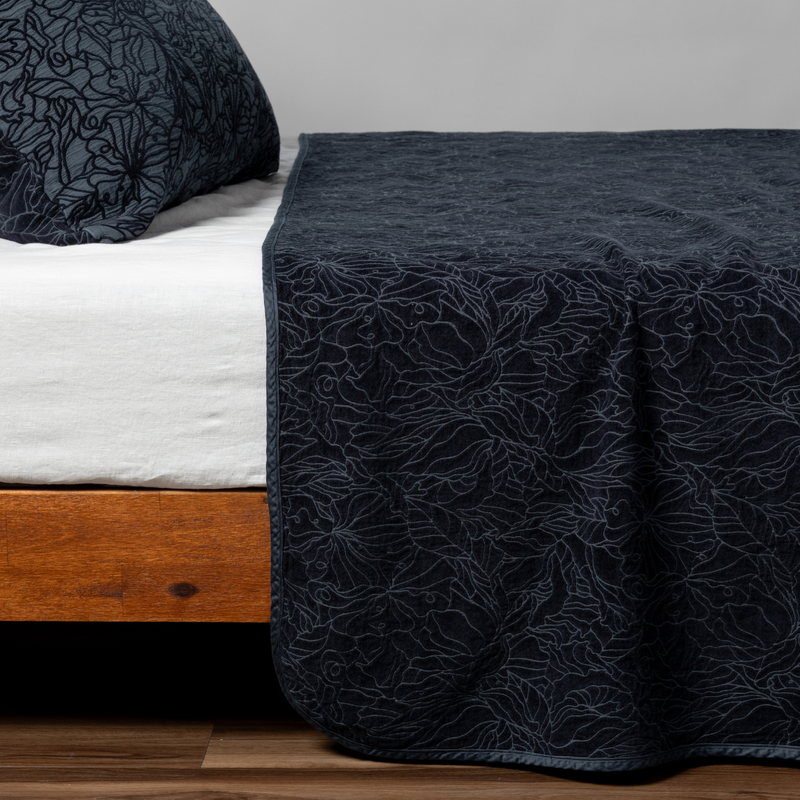 Georgia Twin Bedspread | Slate | Matching Georgia Bedspread and Sham  in slate, a polished dusky dark blue, shown as the sideview on a bed against a plain background.