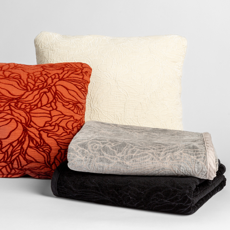 A cluster of two Georgia throw pillows displayed on their cotton jacquard side and two Georgia blankets displayed on their chenille jacquard sides, all against a white background, in the following colorways | one throw pillow in Autumn, a rich terracotta tone, another throw pillow in Winter White, a wooly and warm tone, one blanket in Fog, a neutral mid-grey, and another blanket in Corvino, a raven black tone.