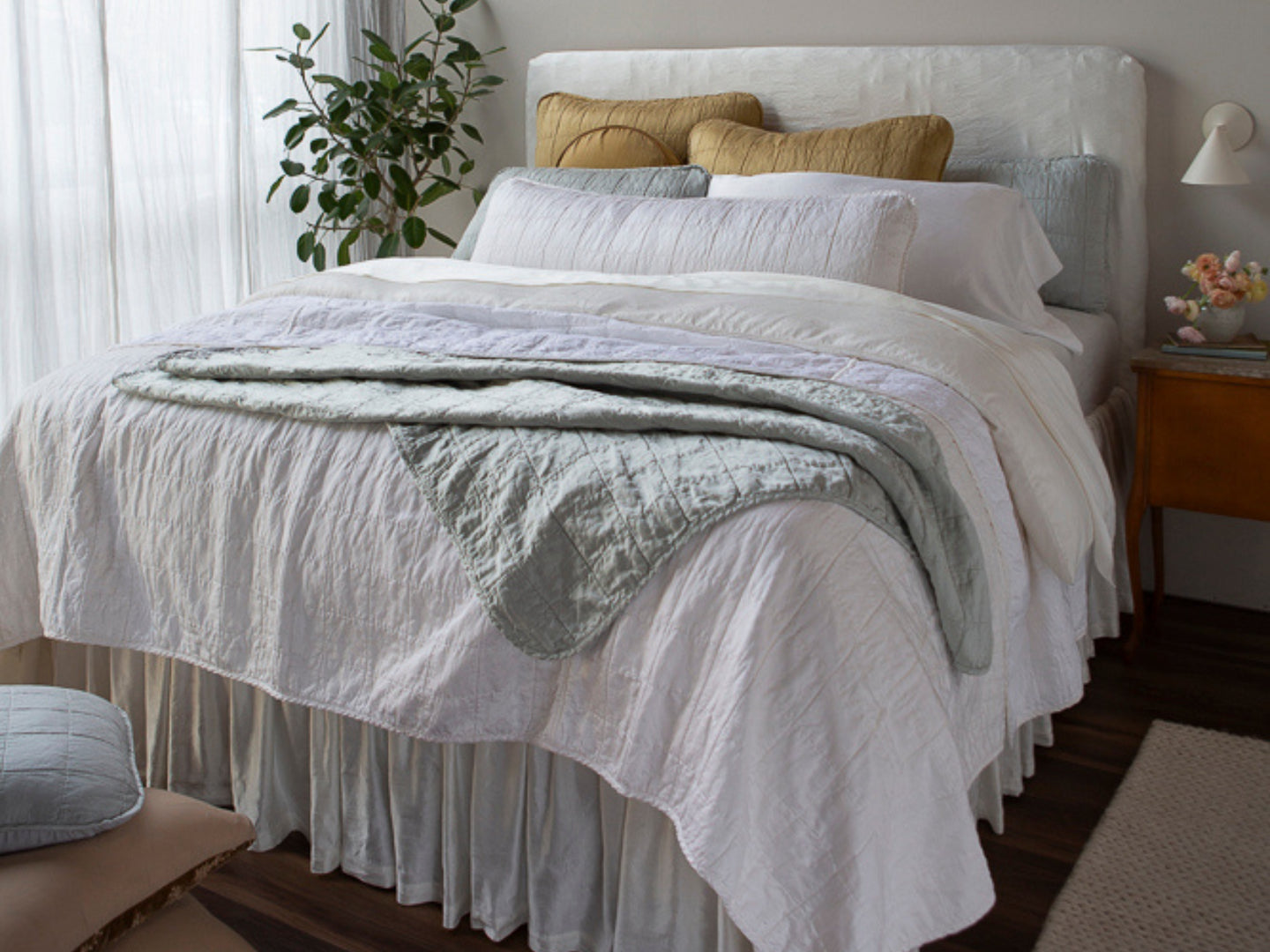 A corner shot of a bed dressed mostly in shades of White with hints of Cloud and Honeycomb. This bed celebrates the addition of Sel to our lineup
of fabric collections. Continue the honeymoon once you’re back
home with this look.
