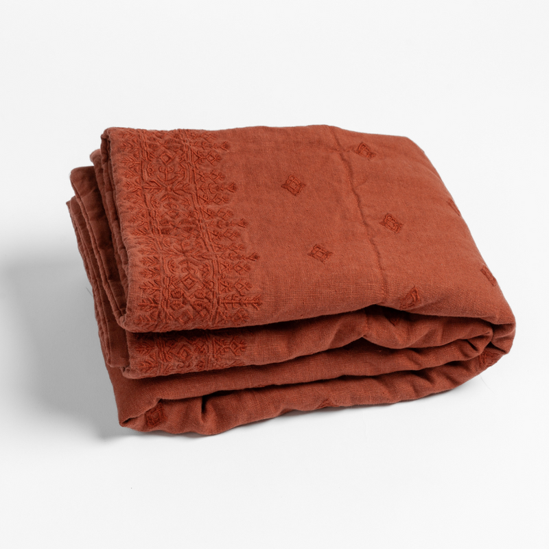 Autumn | A close-up of a folded Ines Baby Blanket with its embroidery pattern shown in Autumn, a rich terracotta tone, shown against a white background.