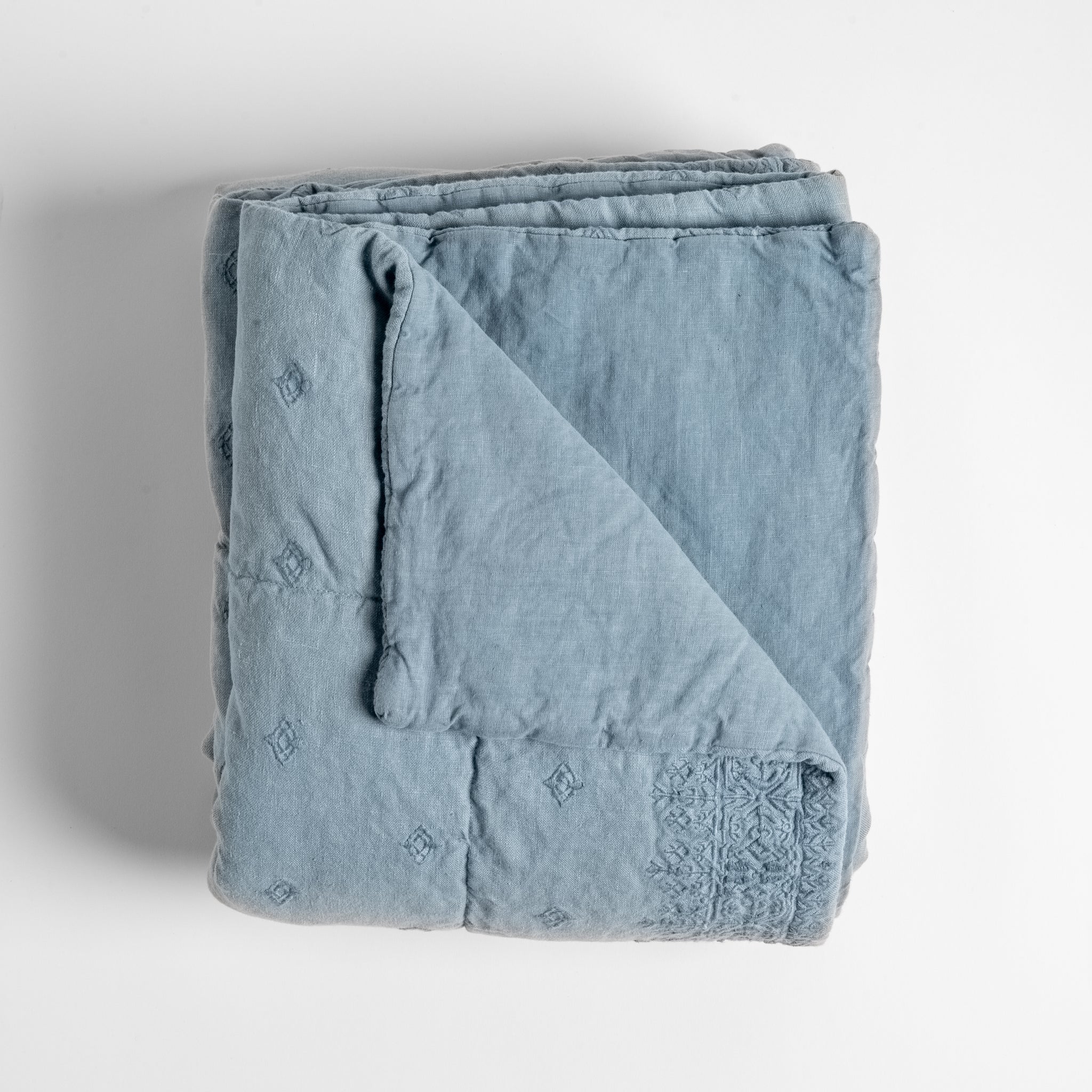 Ines Blanket | Tahoe Blue | Overhead shot of the Ines bedspread folded with a corner showing the inside of the blanket.