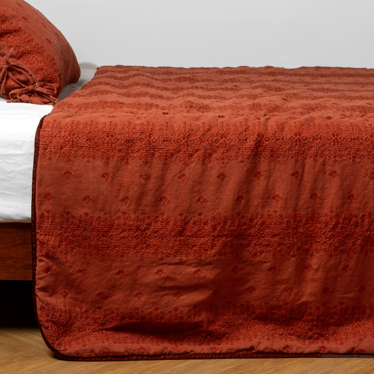 Autumn | A close-up side view of a bed with our Ines Bedspread and a matching pillowcase in Autumn, a rich terracotta tone.