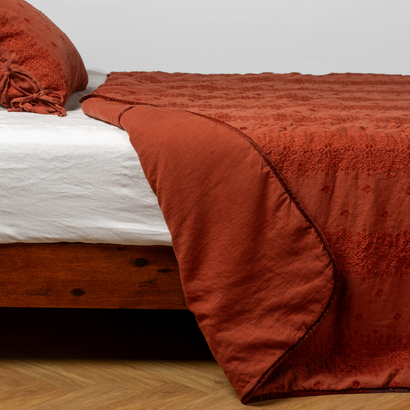 Autumn | A close-up side view of a bed with our Ines Bedspread and a matching pillowcase in Autumn, a rich terracotta tone.