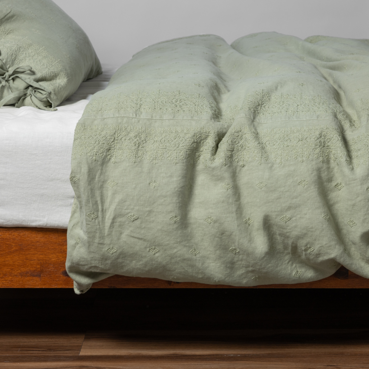Desert Sage | matching ines duvet cover and sham in desert sage, a serenely elegant green, offering a hushed hue, shown from the side on a bed against a plain background.