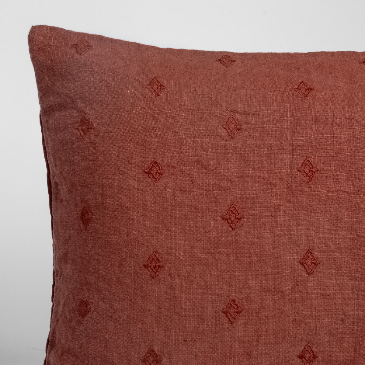 Autumn | A close-up of the corner of an Ines Throw Pillow in Autumn, a rich terracotta tone, shown against a white background.