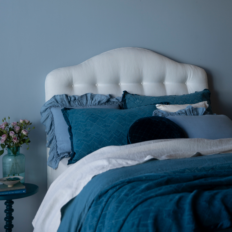 The Trettino Collection | a bed dressed in blue tones against a white curvy headboard and blue wall.