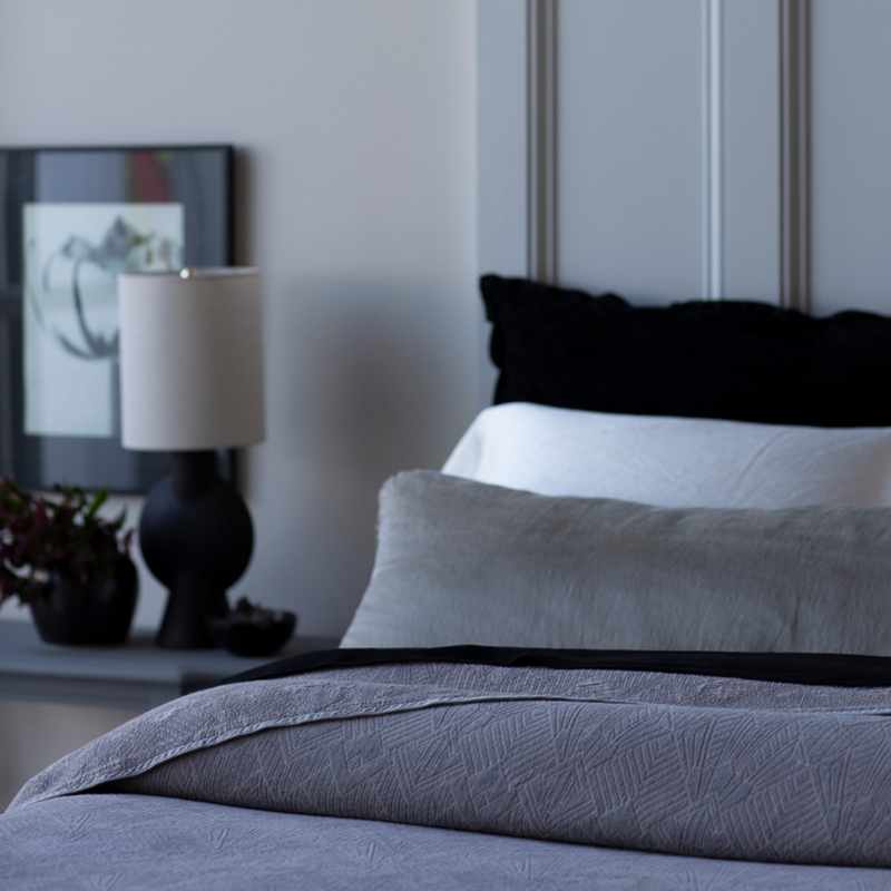 The Trettino Collection | artistic shot across a made bed with the duvet cover subtly folded back, a side table with a lamp and flowers are slightly out of focus in the background.