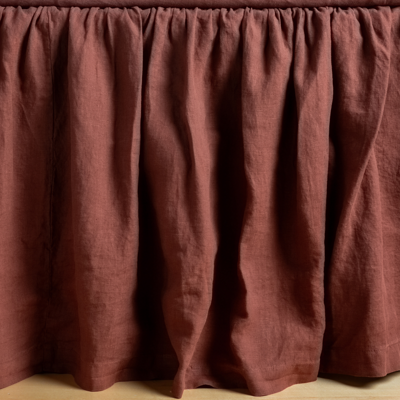 Linen Twin Bed Skirt | Autumn | A close-up side view of a bed with the Linen bed skirt in Autumn, a rich terracotta tone.