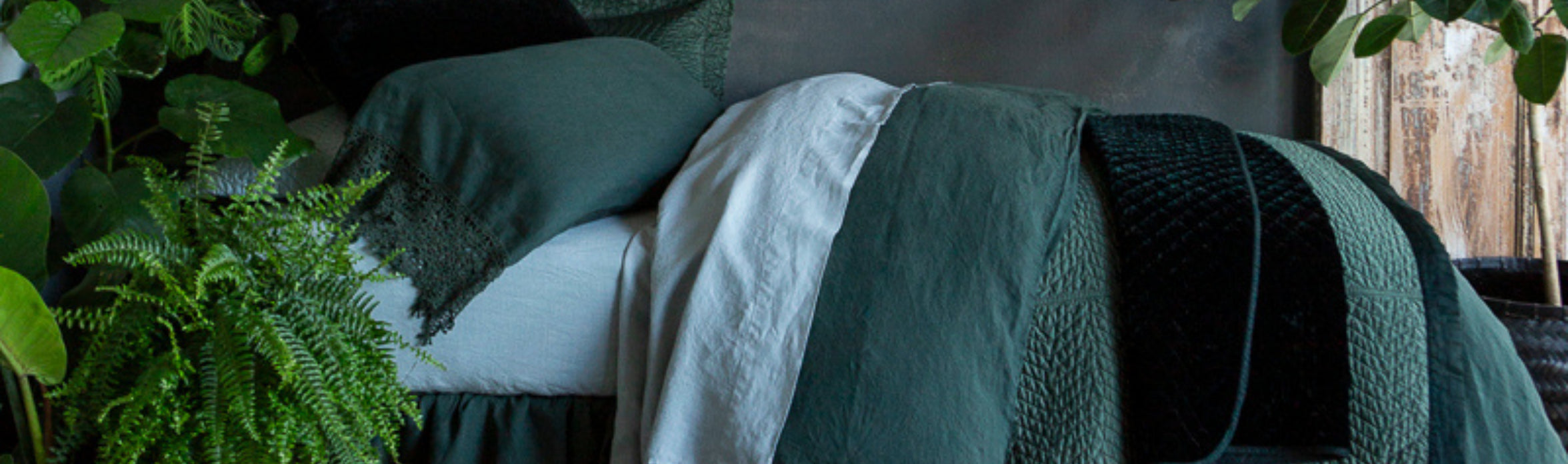 A close up of a green themed bed dressed in the dark juniper hue. plants sit all around the bed. 