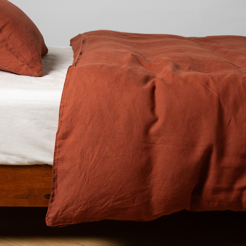 Autumn | A close-up side view of a bed with our Linen Duvet Cover and a matching pillowcase in Autumn, a rich terracotta tone.