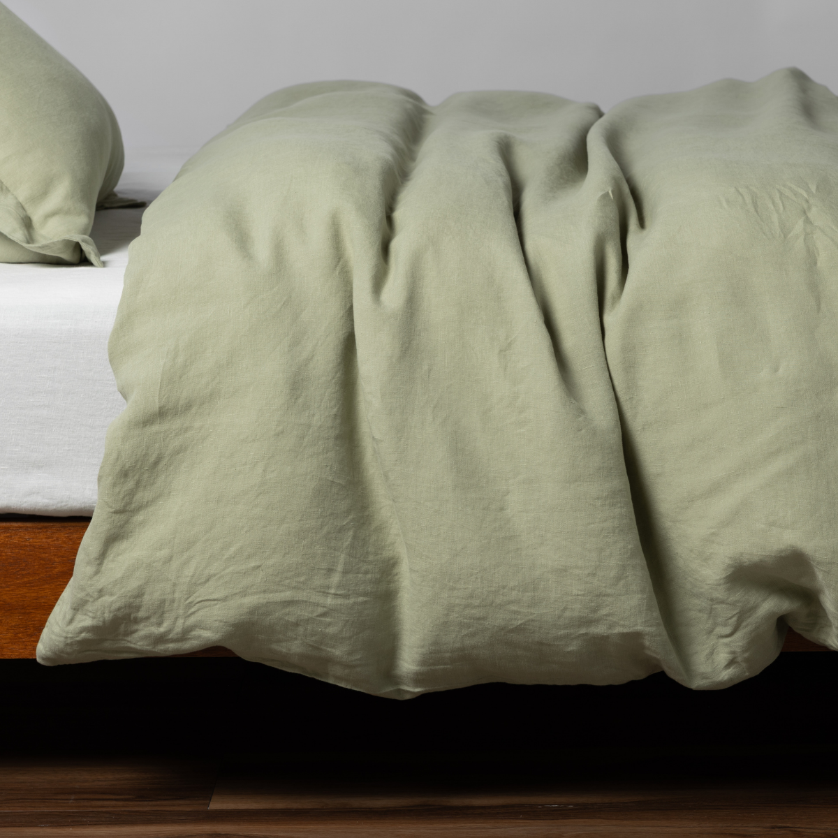 Desert Sage | matching linen duvet cover and sham in desert sage, a serenely elegant green, offering a hushed hue, shown from the side on a bed against a plain background.