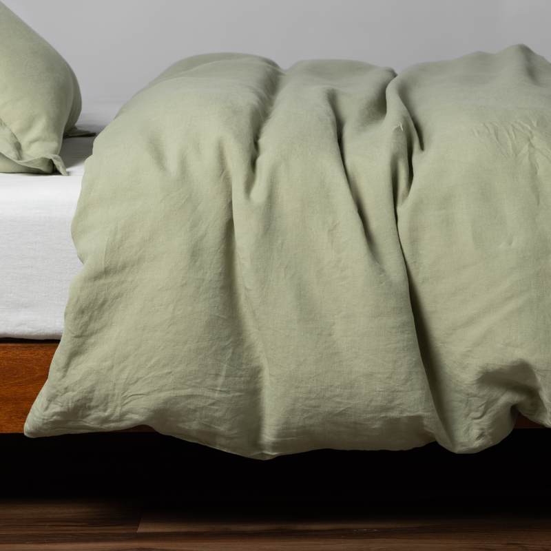 Desert Sage | matching linen duvet cover and sham in desert sage, a serenely elegant green, offering a hushed hue, shown from the side on a bed against a plain background.