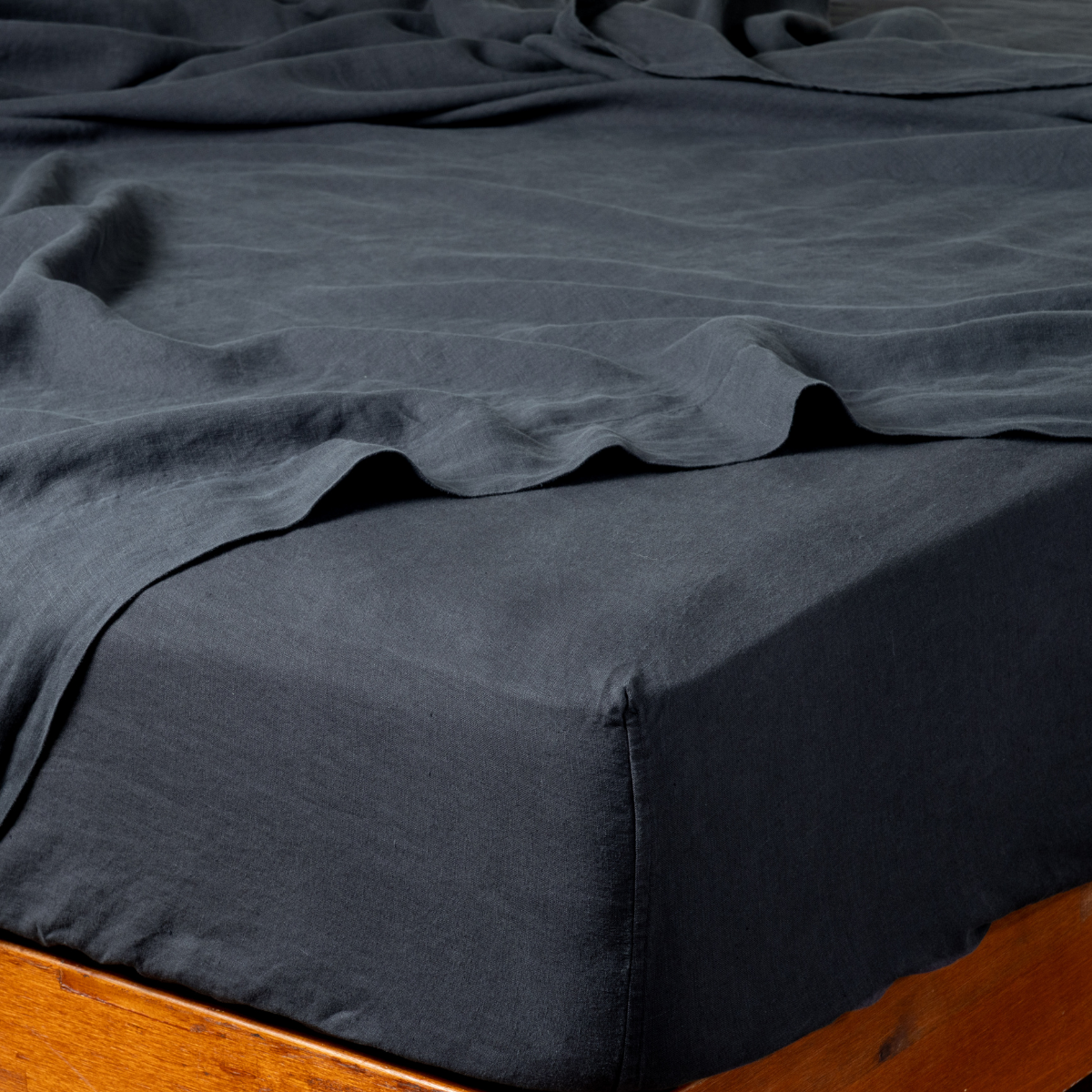 Linen Twin Fitted Sheets | Slate | signature linen fitted sheet on a mattress with its matching flat sheet shown from the corner on a wooden bedframe.