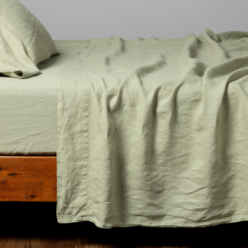 Linen Twin Flat Sheet | Desert Sage | a matching flat sheet, fitted sheet and  pillowcase in desert sage, a serenely elegant green, offering a hushed hue, shown from the side angle on a bed.