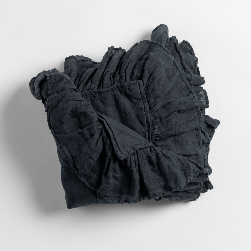Linen Whisper Baby Blanket | Slate | a folded linen with ruffle baaby blanket shown from overhead against a white background.
