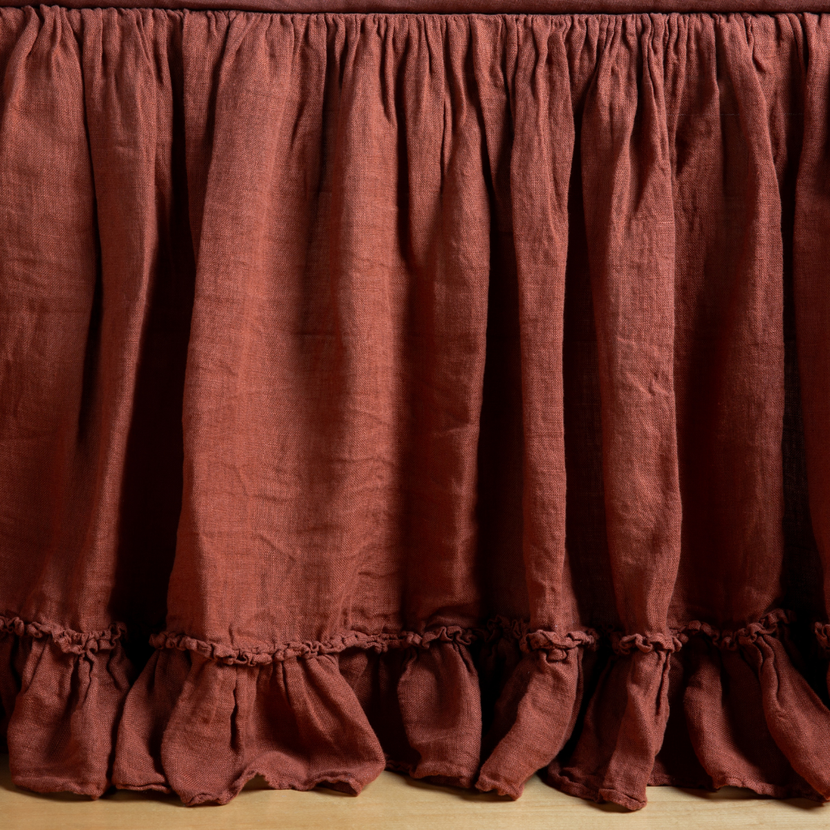 Linen Whisper Bed Skirt | Autumn | A close-up side view of a crib with the Linen Whisper crib skirt in Autumn, a rich terracotta tone.