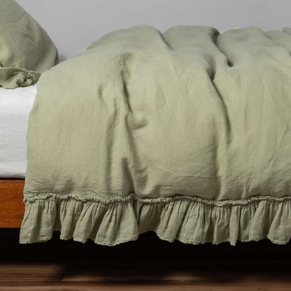 Desert Sage | matching linen whisper duvet cover and pillowcase in desert sage, a serenely elegant green, offering a hushed hue, shown from the side on a bed against a plain background.