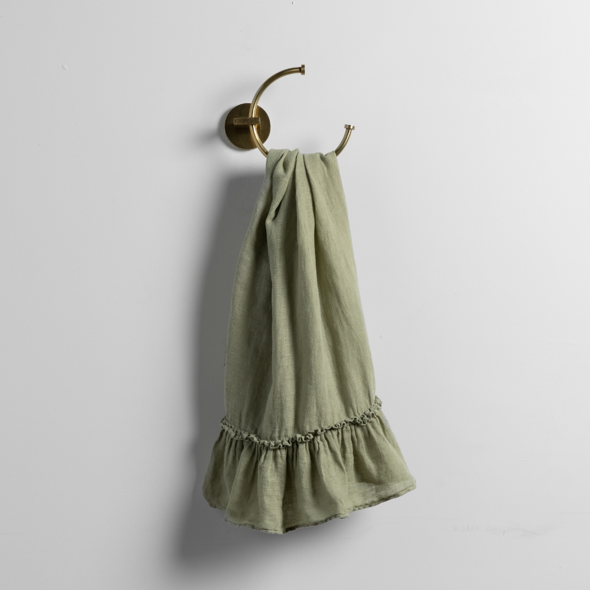 Linen Whisper Guest Towel | Desert Sage | a linen guest towel on a decorative towel ring in desert sage, a serenely elegant green, offering a hushed hue, shown against a plain background.