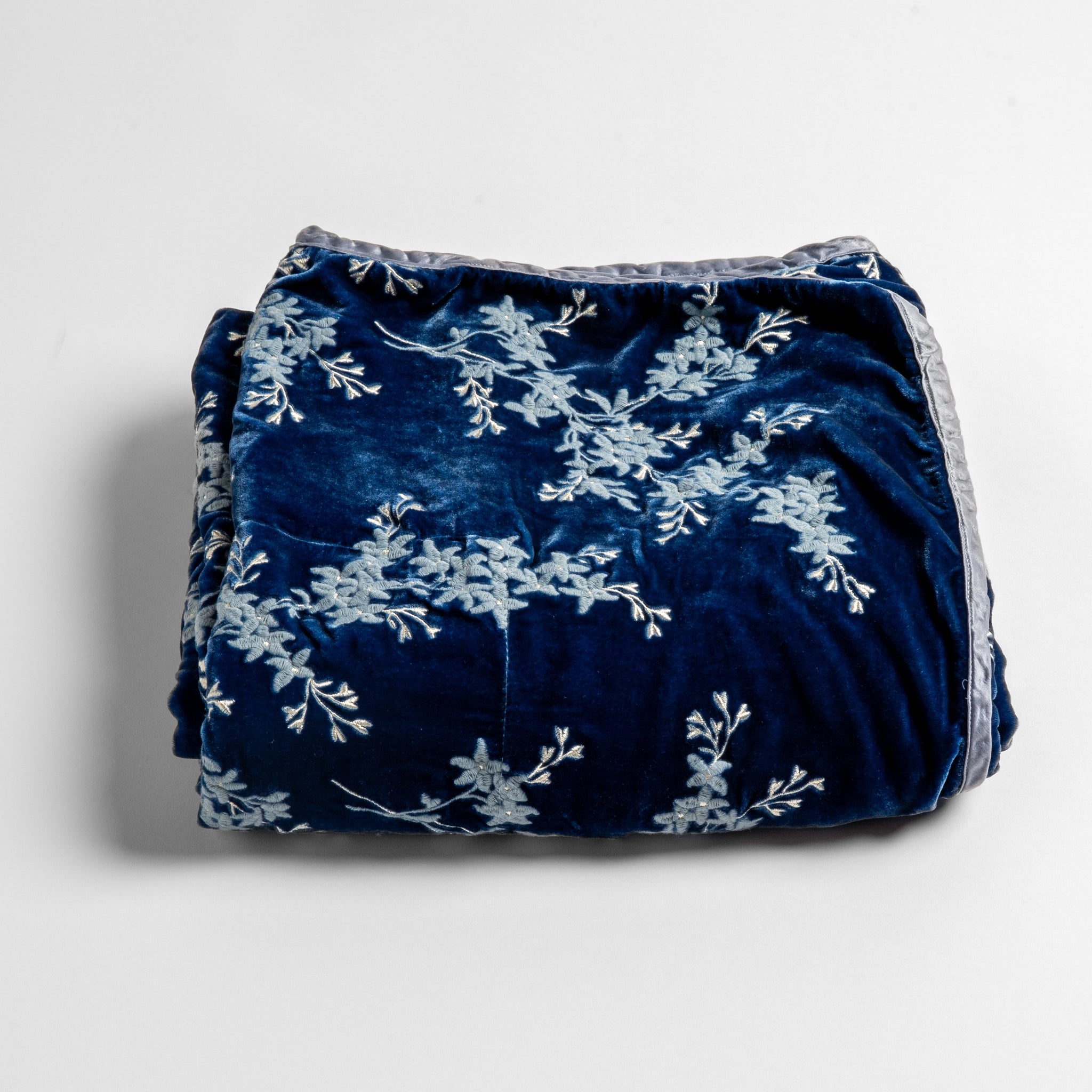 Lynette Baby Blanket | Tahoe Blue | embroidered silk velvet baby blanket folded with a corner folded back to show the trim and back of the blanket - shot overhead at a slight angle against a white background.