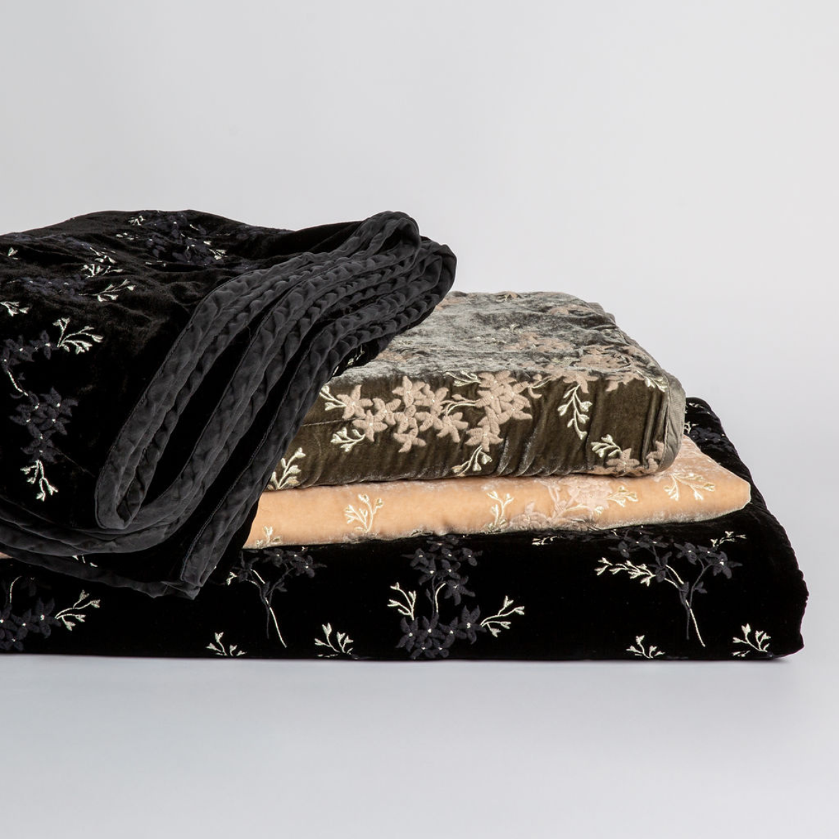 Lynette Blanket | a stack of embroidered silk velvet throw blankets in different colors against a white background.