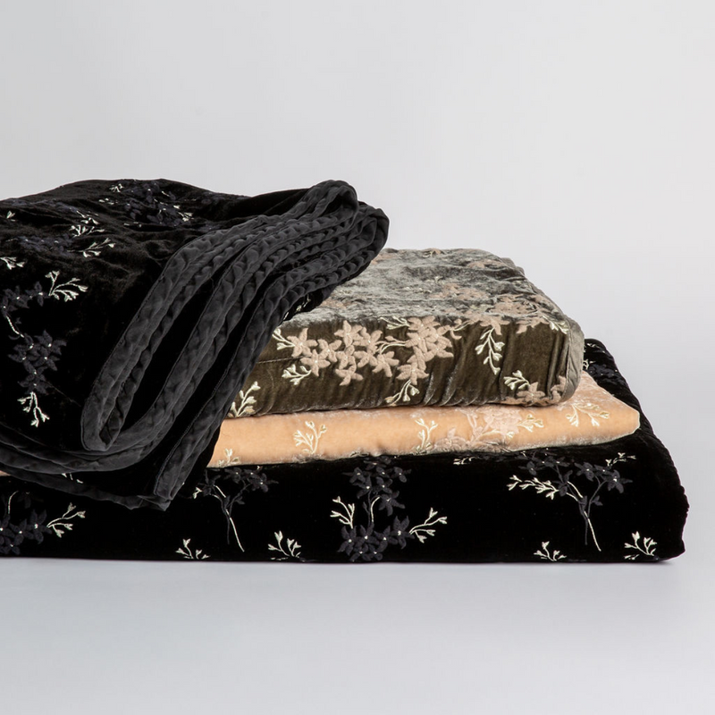 Lynette Blanket | a stack of embroidered silk velvet throw blankets in different colors against a white background.