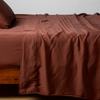 Autumn | A close-up side view of a bed with our Madera Luxe Flat Sheet and a matching pillowcase in Autumn, a rich terracotta tone.