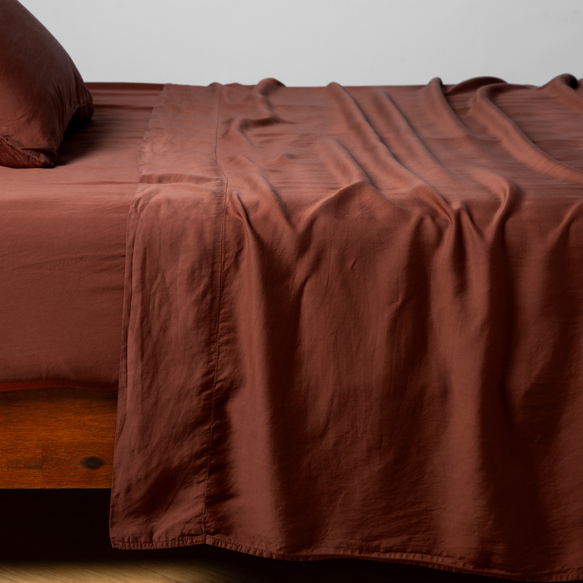 Madera Luxe Fitted Sheet | Autumn | A close-up side view of a bed with our Madera Luxe Flat Sheet and a matching pillowcase in Autumn, a rich terracotta tone.
