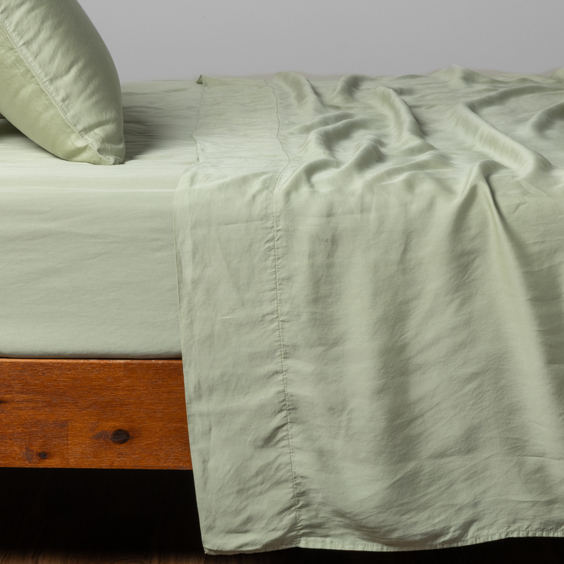 Madera Luxe Twin Flat Sheet | Desert Sage | a matching flat sheet, fitted sheet and  pillowcase in desert sage, a serenely elegant green, offering a hushed hue, shown from the side angle on a bed.