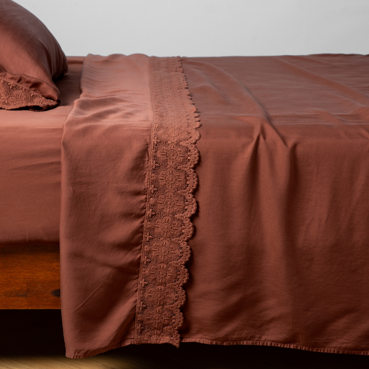 Madera Luxe Flat Sheet | Autumn | A close-up side view of a bed with our Madera Luxe Lace Flat Sheet and a matching pillowcase in Autumn, a rich terracotta tone.