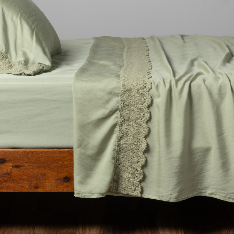 Madera Luxe Flat Sheet | Desert Sage | a matching flat sheet with lace, fitted sheet and  pillowcase in desert sage, a serenely elegant green, offering a hushed hue, shown from the side angle on a bed.