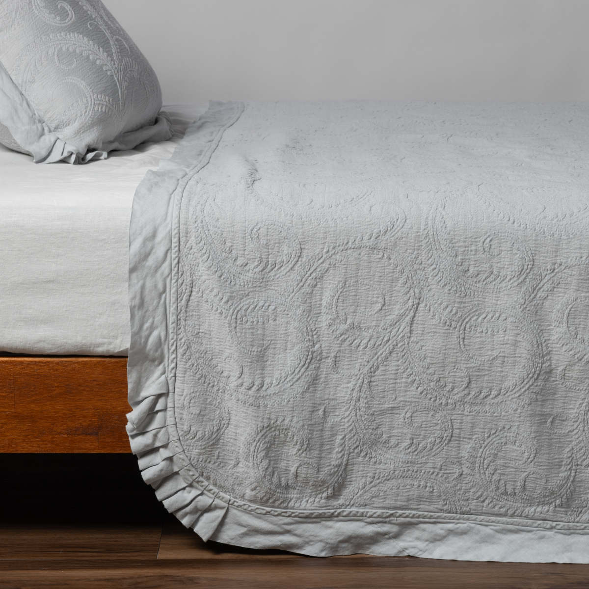 Marisette Bedspread | Cloud | matching organic cotton damask trimmed with linen bedspread and sham on a bed with white fitted sheet, shown from the side against a plain background.