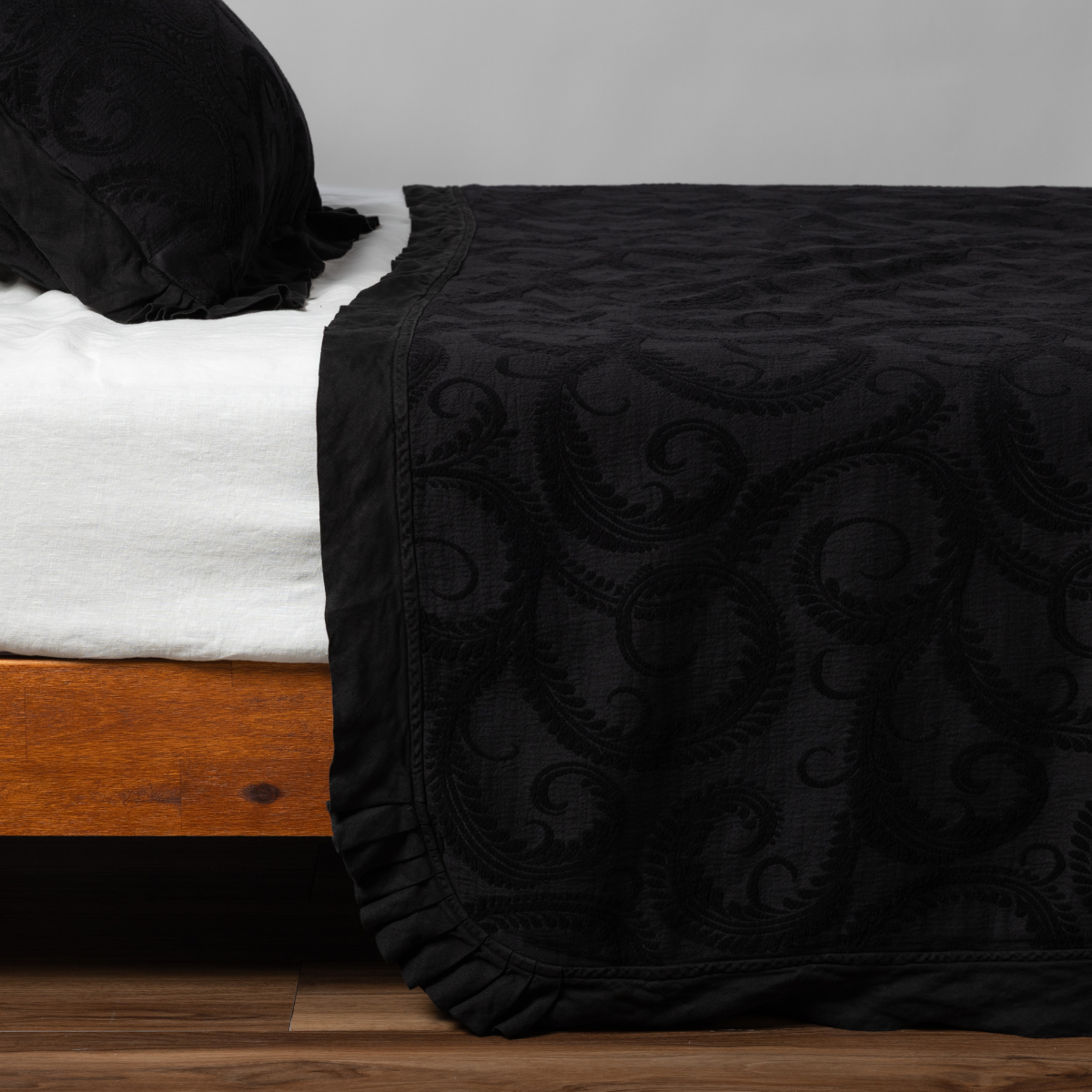 Marisette Bedspread | Corvino | matching organic cotton damask trimmed with linen bedspread and sham on a bed with white fitted sheet, shown from the side against a plain background.