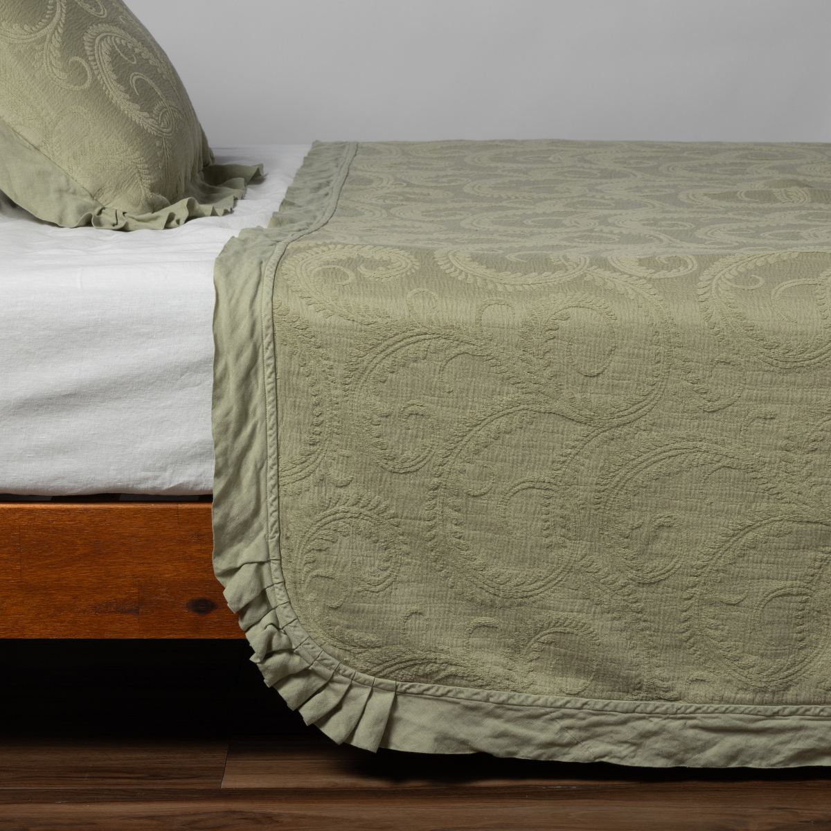 Marisette Bedspread | Desert Sage | matching marisette coverlet and sham in desert sage, a serenely elegant green, offering a hushed hue, shown from the side on a bed against a plain background.