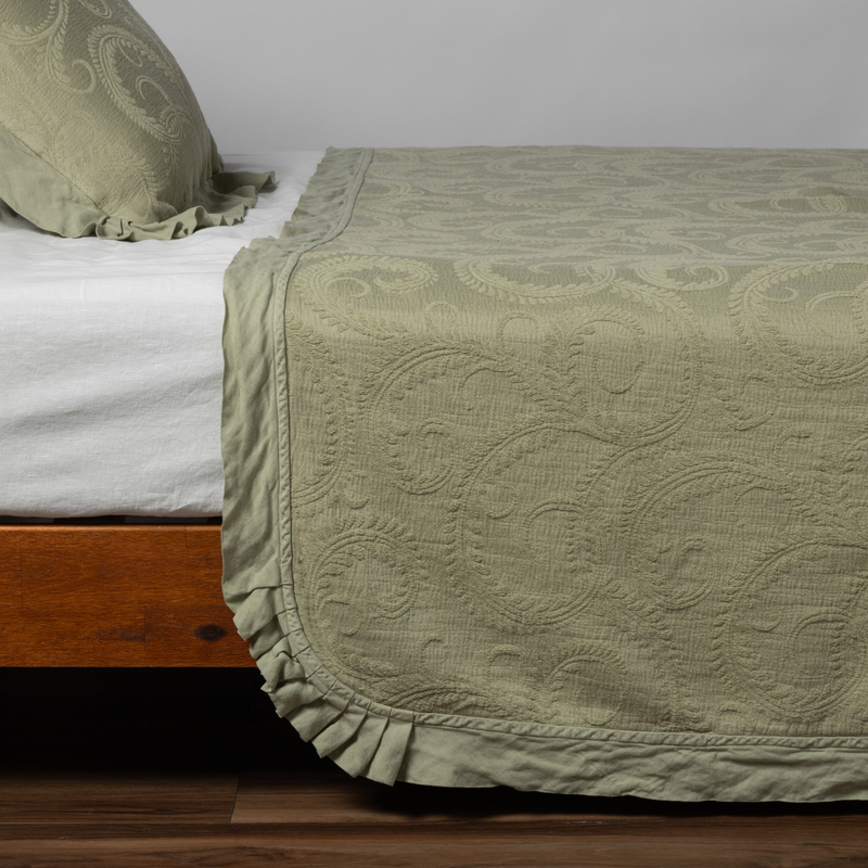 Marisette Bedspread | Desert Sage | matching marisette coverlet and sham in desert sage, a serenely elegant green, offering a hushed hue, shown from the side on a bed against a plain background.