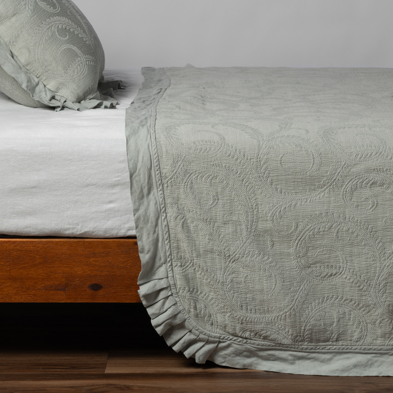 Marisette Bedspread | Eucalyptus | matching organic cotton damask trimmed with linen bedspread and sham on a bed with white fitted sheet, shown from the side against a plain background.
