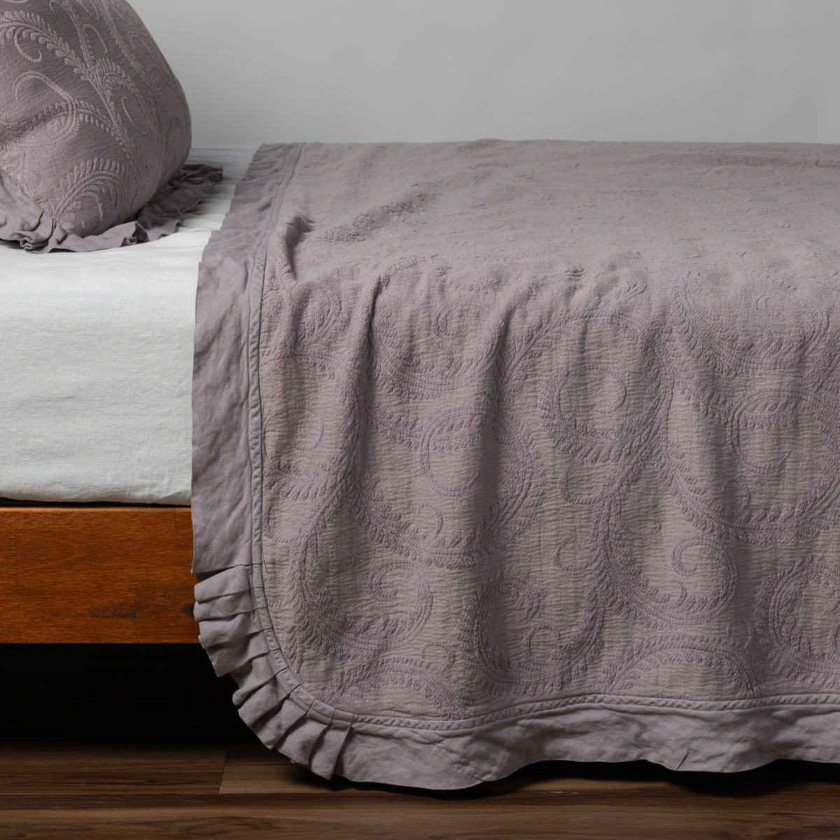 Marisette Bedspread | French Lavender | matching organic cotton damask trimmed with linen bedspread and sham on a bed with white fitted sheet, shown from the side against a plain background.