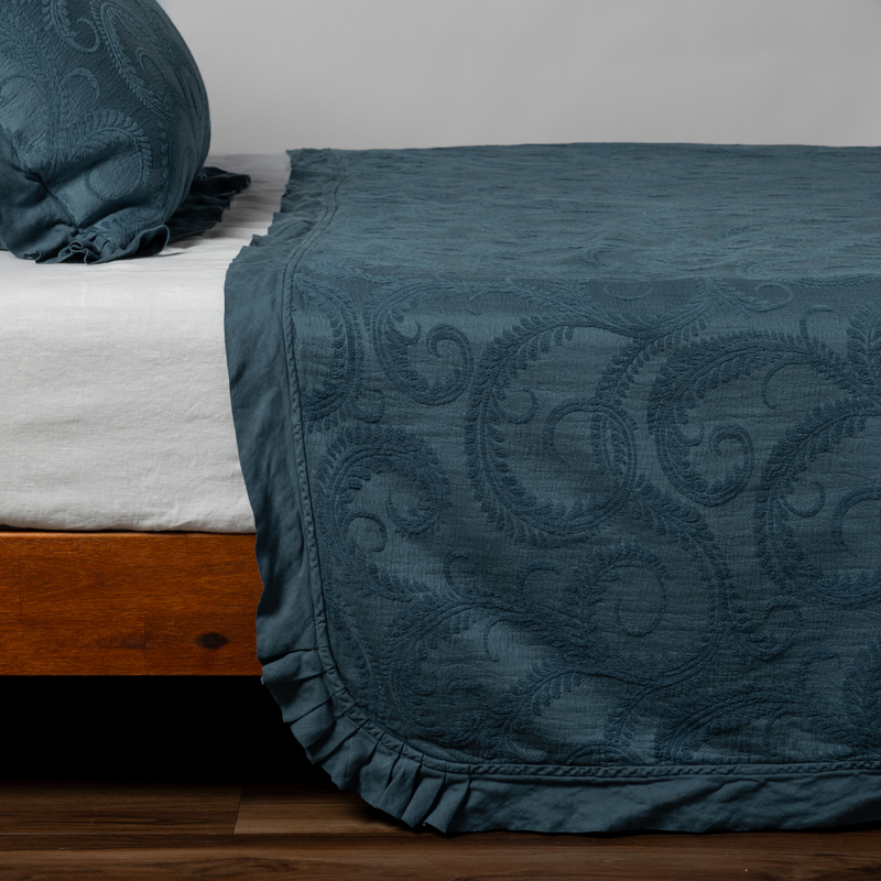 Marisette Bedspread | Midnight | matching organic cotton damask trimmed with linen bedspread and sham on a bed with white fitted sheet, shown from the side against a plain background.
