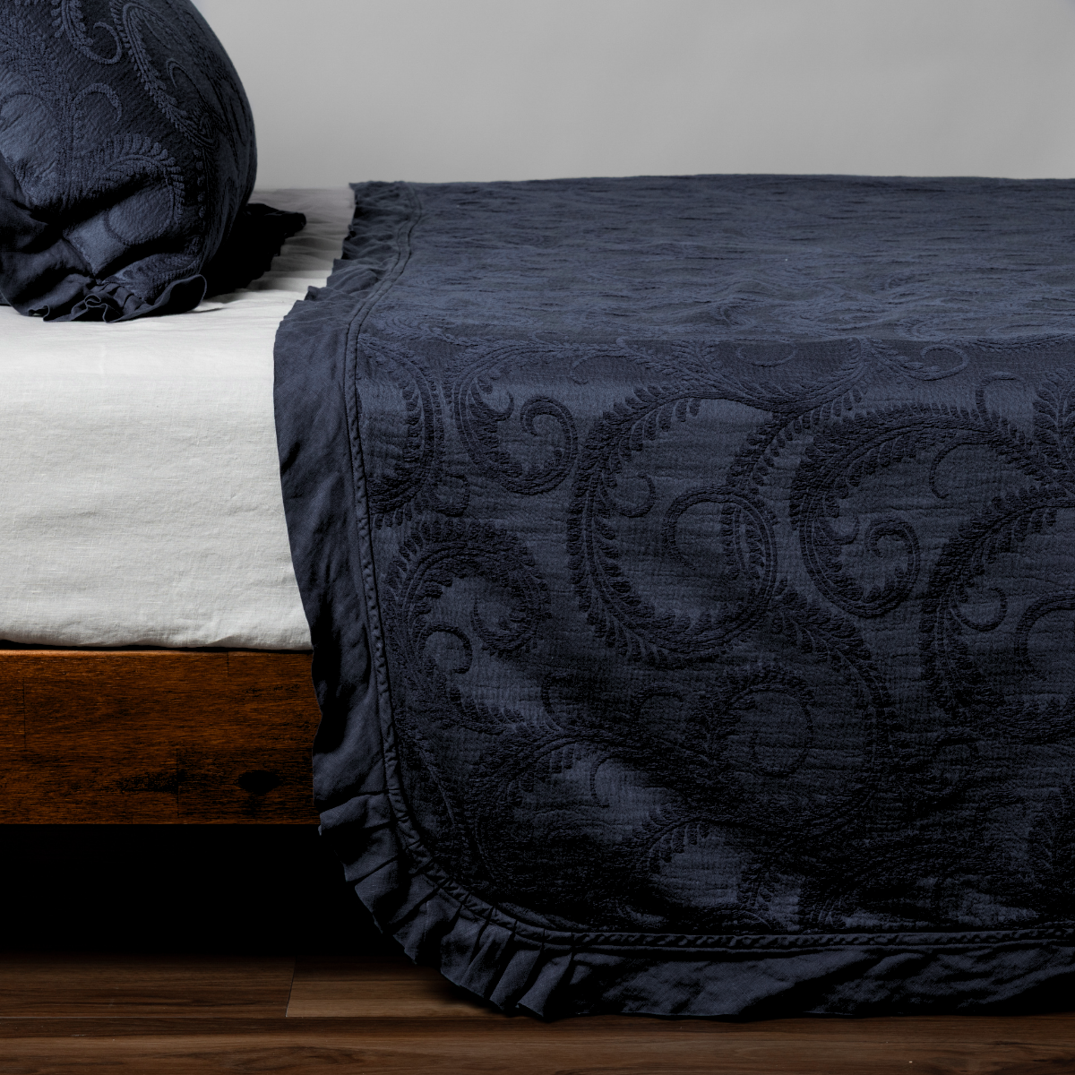 Marisette Bedspread | Slate | matching organic cotton damask trimmed with linen bedspread and sham on a bed with white fitted sheet, shown from the side against a plain background.