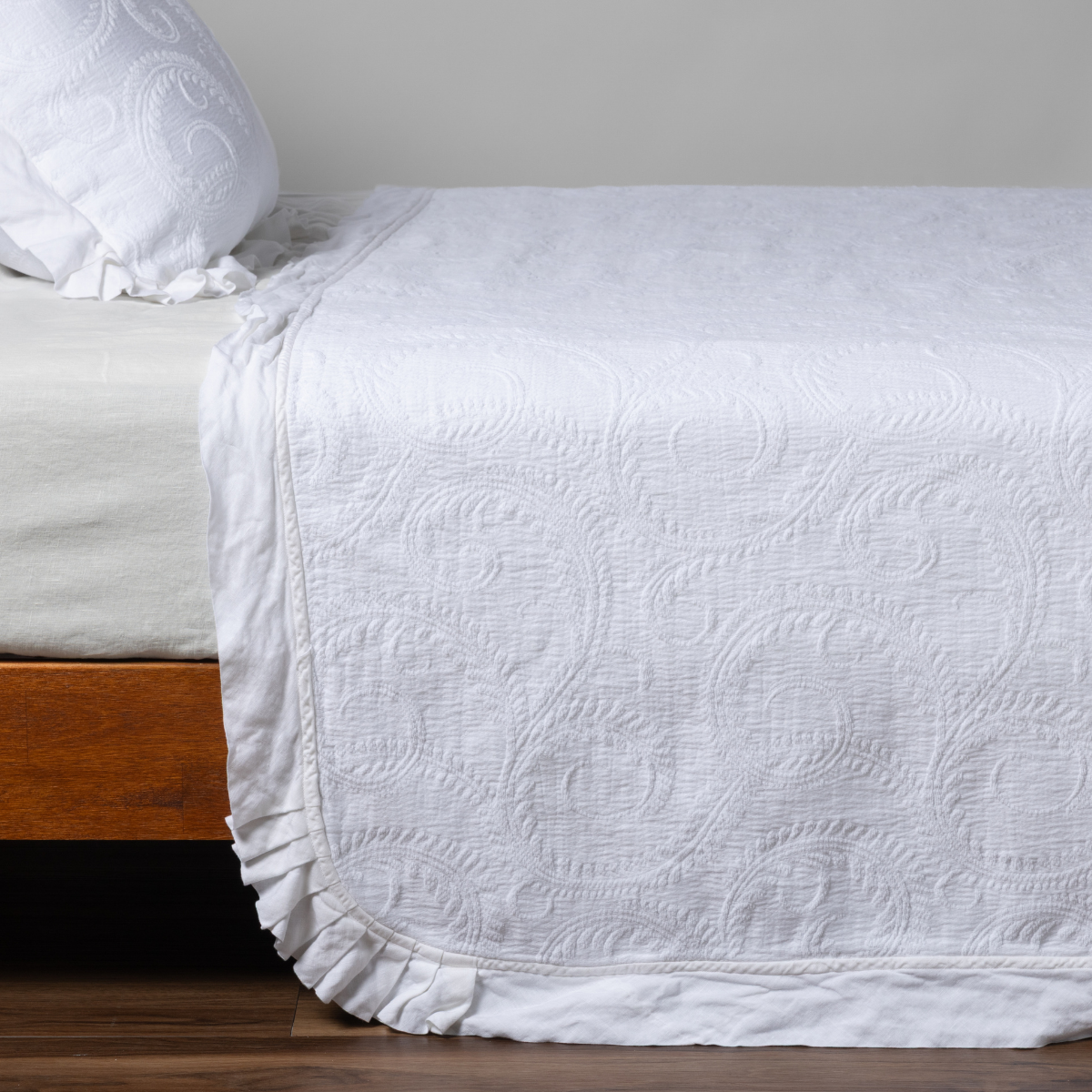 Marisette Bedspread | White | matching organic cotton damask trimmed with linen bedspread and sham on a bed with white fitted sheet, shown from the side against a plain background.